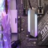 A close-up of a computer motherboard featuring a gray heatsink and colorful lighting accents.